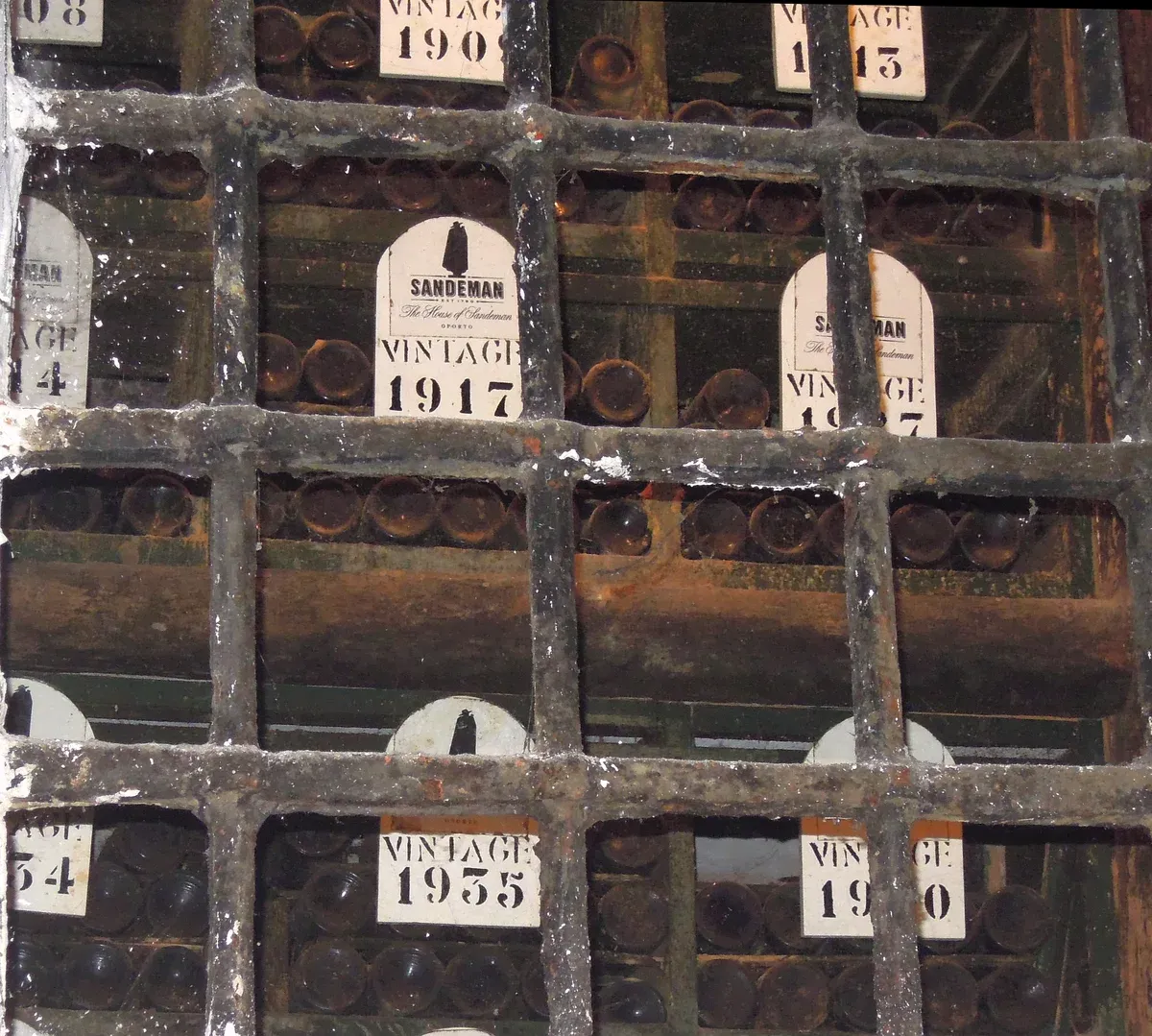 Old vintage port bottles behind a grille in a Porto cellar, seen on a port wine cellar tour in Vila Nova de Gaia